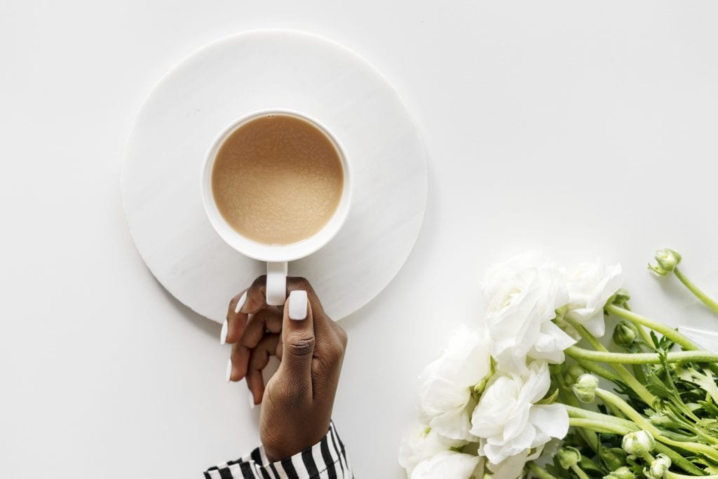 Coffee cup held by a person with white flowers on the side, minimalistic white background.
