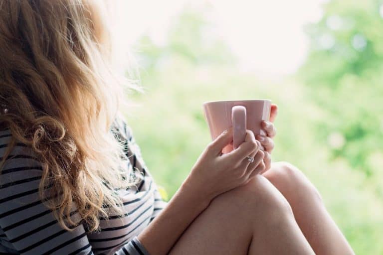 Woman sitting on windowsill holding coffee cup